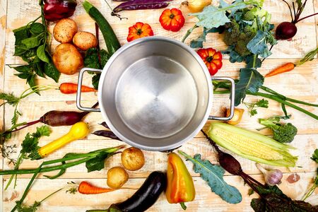 Various organic vegetables ingredients around empty cooking pot on old wooden table, top view. Flat...
