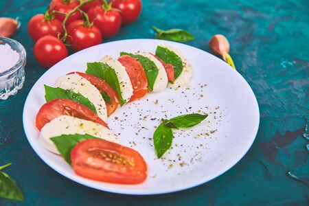 Italian caprese salad with sliced tomatoes, mozzarella cheese, basil, olive oil om green background....