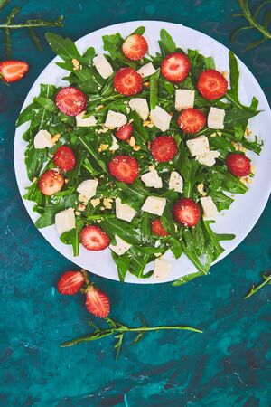 Fresh salad with arugula, strawberries, feta cheese and nuts on green background. Vegetarian. Diet food. Italian food. Top view. Copy space.の写真素材