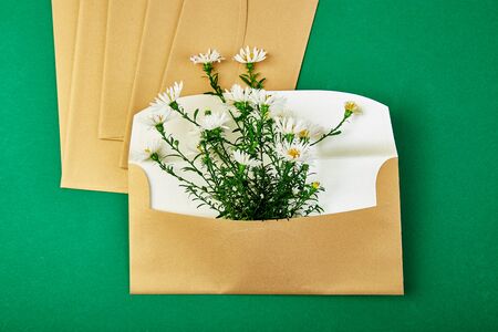 Gold envelope with a spring flower arrangement on green background. Flat lay, top view. Opened envelope. Festive greeting conceptの写真素材