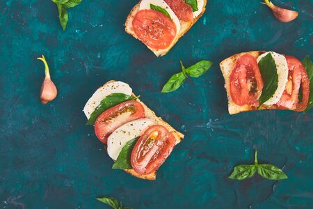 Caprese bruschetta toasts. Bruschetta with tomatoes, mozzarella cheese and basil on a green background. Traditional italian appetizer or snack, antipastoの写真素材