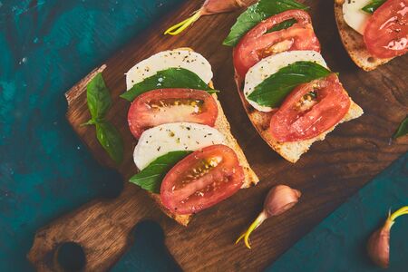 Caprese bruschetta toasts on cutting board. Bruschetta with tomatoes, mozzarella cheese and basil on a green background. Traditional italian appetizer or snack, antipastoの写真素材