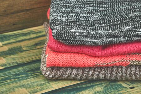 Stack of cozy knitted sweaters. A pile of warm sweaters on a wooden table on green rustic background. Autumn and winter clothes. Copy space.の写真素材