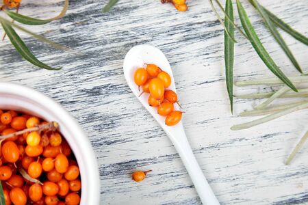 Natural, organic sea buckthorn berry in bowl and a on white wooden background. Branch of sea buckthorn. Top view.の写真素材
