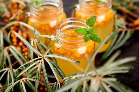 Vitaminic healthy sea buckthorn tea in small glass cups with fresh raw sea buckthorn berries, honey on black backgroundの写真素材