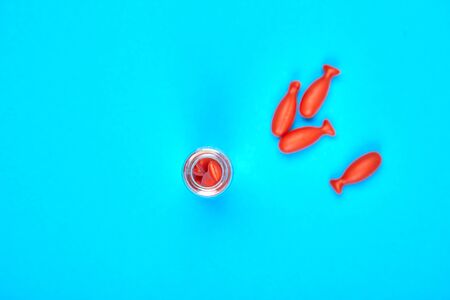 Minimalism style Omega 3 fish capsules spilling out of glass bottle on a blue background. Flat lay