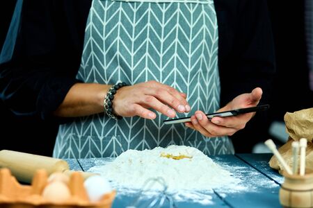 Man using electronic tablet pc in kitchen for baking. Man searching for food recipe in tablet computer. Close up man touching tablet screen and browsing recipes.の写真素材