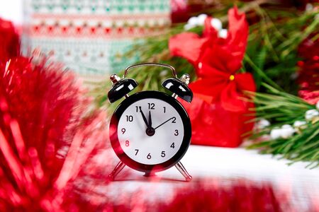 Black Alarm clock and fir tree branch, red christmas decorations on white wooden  background. Eve Time Concept on table. New Year is coming. Christmas gift card.の写真素材