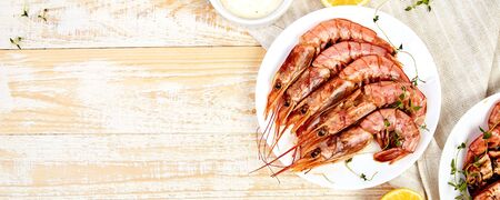 Banner with Grilled big tiger shrimps prawns on white plate with spices, lemon, fresh herbs on white wooden background, top view. Grilled seafood. Barbecue shrimps. Copy space.の写真素材