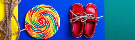 Banner with Small red boat shoes near big multi-colored lollipop and rope on colored background. Top...