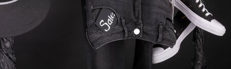Banner with Sale sign, Black and white snaekers, cap and pant, jeans hanging on clothes rack on black background. Black friday. Close up.の写真素材