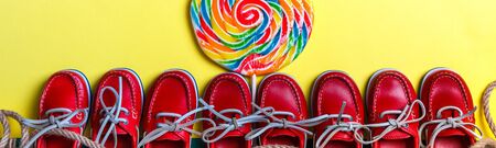 Banner with A lot of small red boat shoes near big multi-colored lollipop on colored background. Top view, copy space. Frame. group of child boat shoes.の写真素材