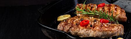 Banner with Grilled pork steak in grill pan with rosemary, pepper chilli and ginger on wooden board. Copy space.の写真素材