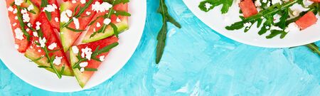 Banner of Fresh summer watermelon salad with feta cheese and arugula on blue table background. Vegan food. Diet, Vegetarian. Top view. Flat lay. Copy spaceの写真素材