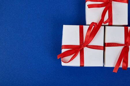 Luxury white gift boxes with red ribbon on blue trend color background. Valentine Day, Christmas,...