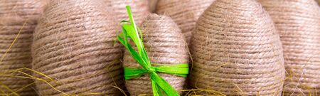 Banner of Easter eggs wrapped in twine in yellow nest on wooden sackcloth wooden background. Rustic...