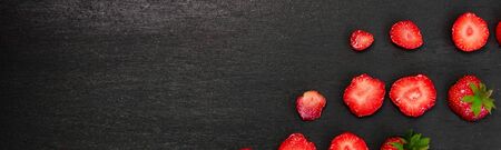 Banner of Sliced strawberries with leaves on black background. Top view, frame. Copy space. Summer fruit food frame. Flat layの写真素材
