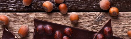 Banner of Chocolate pieces with hazelnut nuts on wooden background. Top view. Copy space. Frameの写真素材