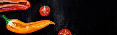 Banner of Mixed of half red and yellow pepper with a green branch near cherry tomato on a black backround. Top view. Frame. Copy space. Flat layの写真素材