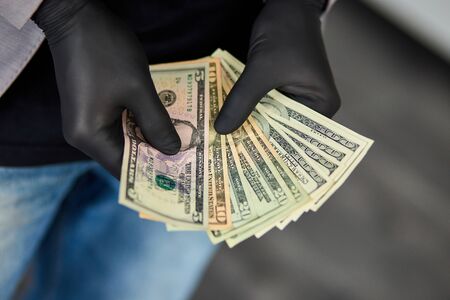 Man holding money dollars in hand in black medical gloves. Coronavirus crisis. Save money.の写真素材