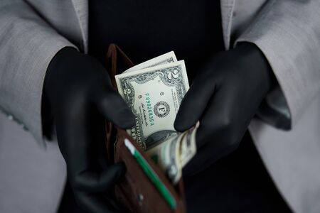 Man holding a wallet with money dollars in hand in black medical gloves.