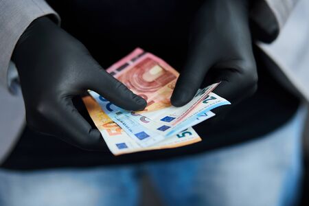 Man holding a wallet with money euro in hand in black medical gloves. Coronavirus crisis. Save money. The world crisisの写真素材