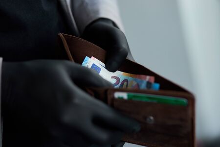 Man holding a wallet with money euro in hand in black medical gloves. Coronavirus crisis. Save...