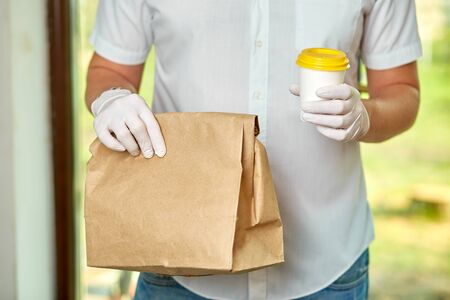 Courier, delivery man in protective mask and medical gloves delivers takeaway food and coffee....