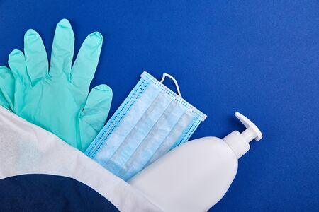 Protective medical mask, sanitizer gel and gloves in white bag on blue background. Protective...