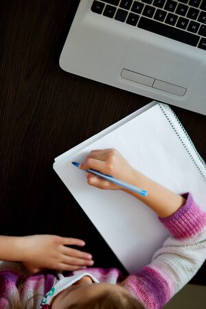 Unrecognizable schoolgirl studying at home with a notebook and doing school homework. Distance...