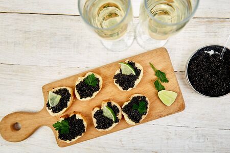 Sandwiches with black caviar. Sturgeon black caviar in wooden bowl, sandwiches and champagne on white background copy space. Top view.の写真素材