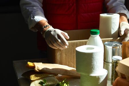 Volunteer in the protective medical mask and gloves putting food In donation box.