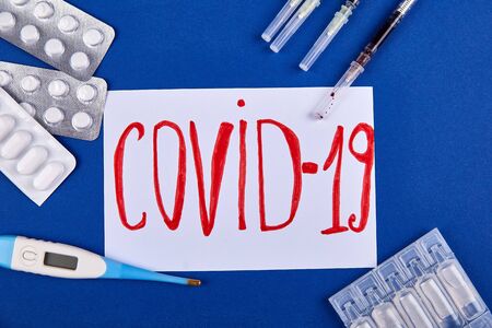 The inscription Covid-19 of tablets, tablets and a thermometer on a blue background. Human life and...
