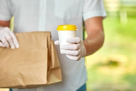 Courier, delivery man in protective mask and medical gloves delivers takeaway food and coffee....