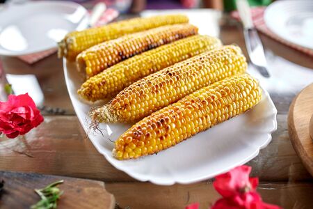 Grilled corn cobs on plate on the dinner table, appetizers variety serving on party outdoor table at...