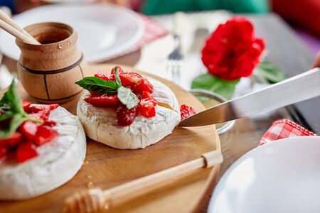 Man cut grilled camembert cheese with strawberry, honey and basil leaves, delicatessen, camembert cheese fondue on the dinner table.の写真素材