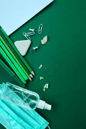 Flat lay schooling after the pandemic, Back to school in a new reality, School supplies, protective mask and antiseptic on a green background, space for text.の写真素材