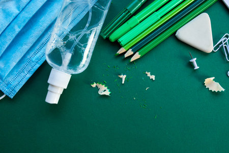 Flat lay schooling after the pandemic, Back to school in a new reality, School supplies, protective mask and antiseptic on a green background,  space for text.の写真素材