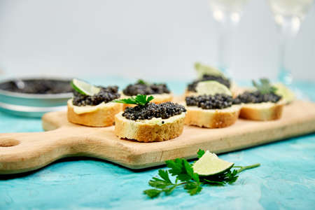Sturgeon black caviar in wooden bowl, sandwiches and champagne on white background copy space.
