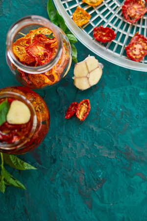Homemade sun dried tomatoes with herbs, garlic in olive oil in a glass jar on dark green background. Top view. Print for kitchenの写真素材