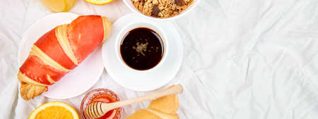 Good morning. Banner of Continental breakfast on white bed sheets. Cup of coffee, orange juice, croissants, jam muesli, granola, from above. Top view. Flat lay. Copy spaceの写真素材