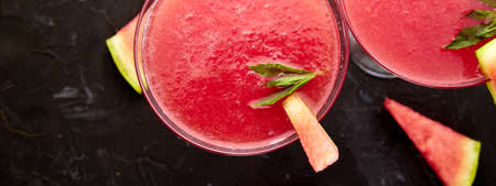 Watermelon margarita cocktail on black background. Fresh watermelon lemonade with mint and ice for summer party. Refreshing summer drink. Top view.の写真素材