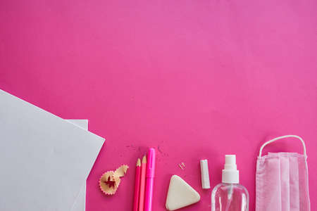 Flat lay schooling after the pandemic, Back to school in a new reality, School supplies, protective mask and antiseptic on a pink background, space for text.の写真素材