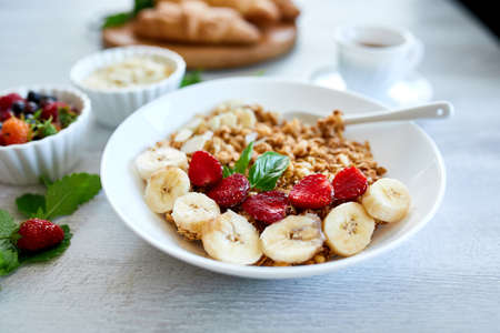 Healthy breakfast bowl, fresh granola, muesli with yogurt fruits and coffee, strawberry, banana on...