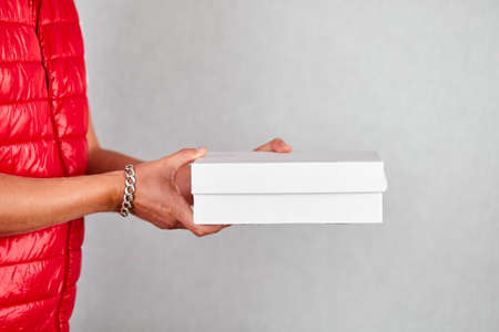 Delivery man employee in red vest uniform hold empty cardboard box isolated on grey background...