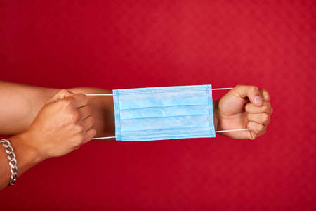 Men Hand holding a protection medical mask on red studio background