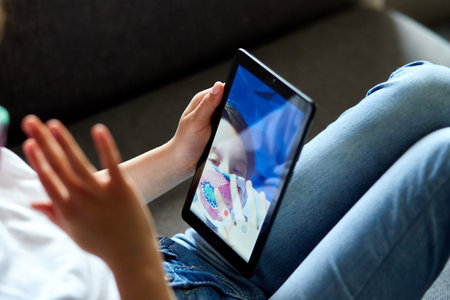 Little child girl in mask at home talk video with tablet meeting, online call friend