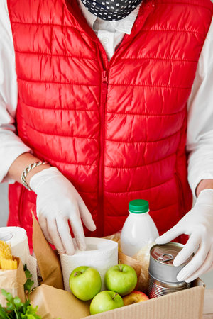 Volunteer in the protective medical mask and gloves putting food In donation box.