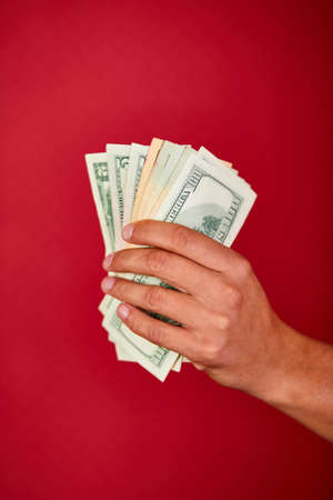 Mans hand holding and showing dollars banknote money isolated on red background