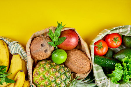 Flat lay of eco friendly grocery shopping cotton bags with organic fruits and vegetable on yellow background. Zero waste, plastic free lifestyle concept. Healthy veggie food diet and detox.の写真素材